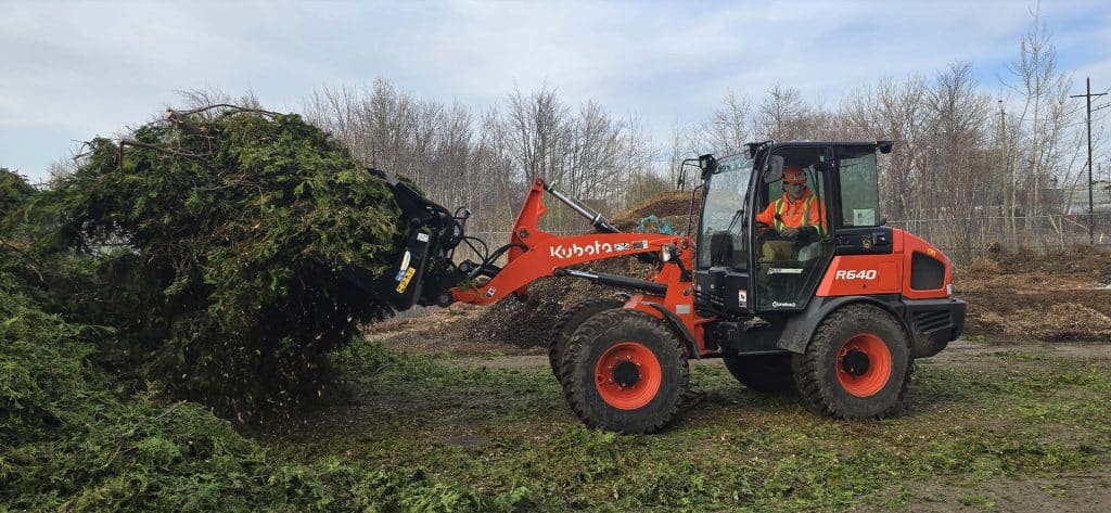 Opérateur utilisant un chargeur Kubota R640 pour déplacer des résidus verts fraîchement broyés sur un site de compostage au Québec.