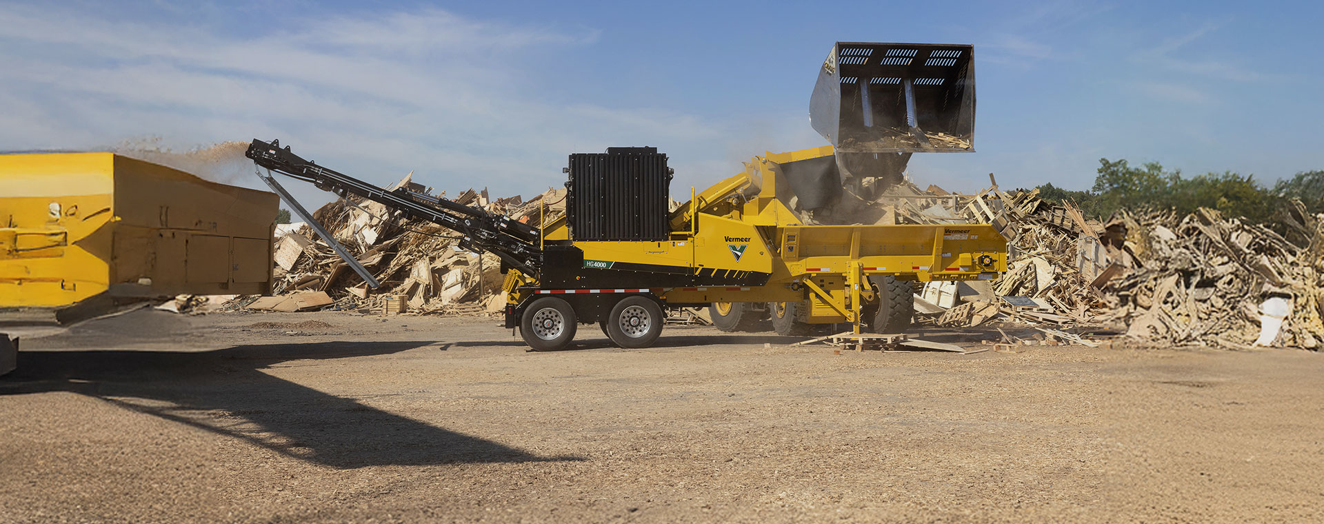 Chargeuse déversant des débris de bois dans un broyeur industriel Vermeer HG4000 sur un site de recyclage de matériaux de construction