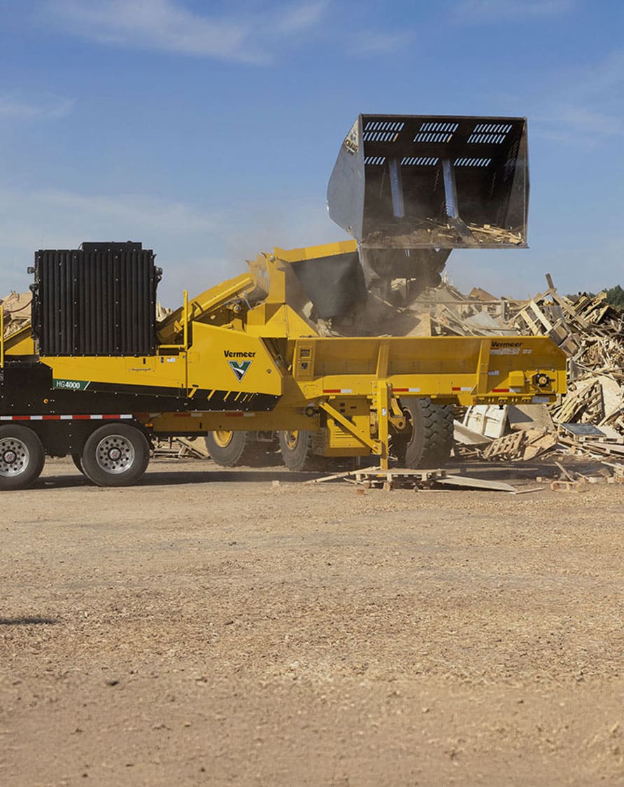 Chargeuse déversant des débris de bois dans un broyeur industriel Vermeer HG4000 sur un site de recyclage de matériaux de construction